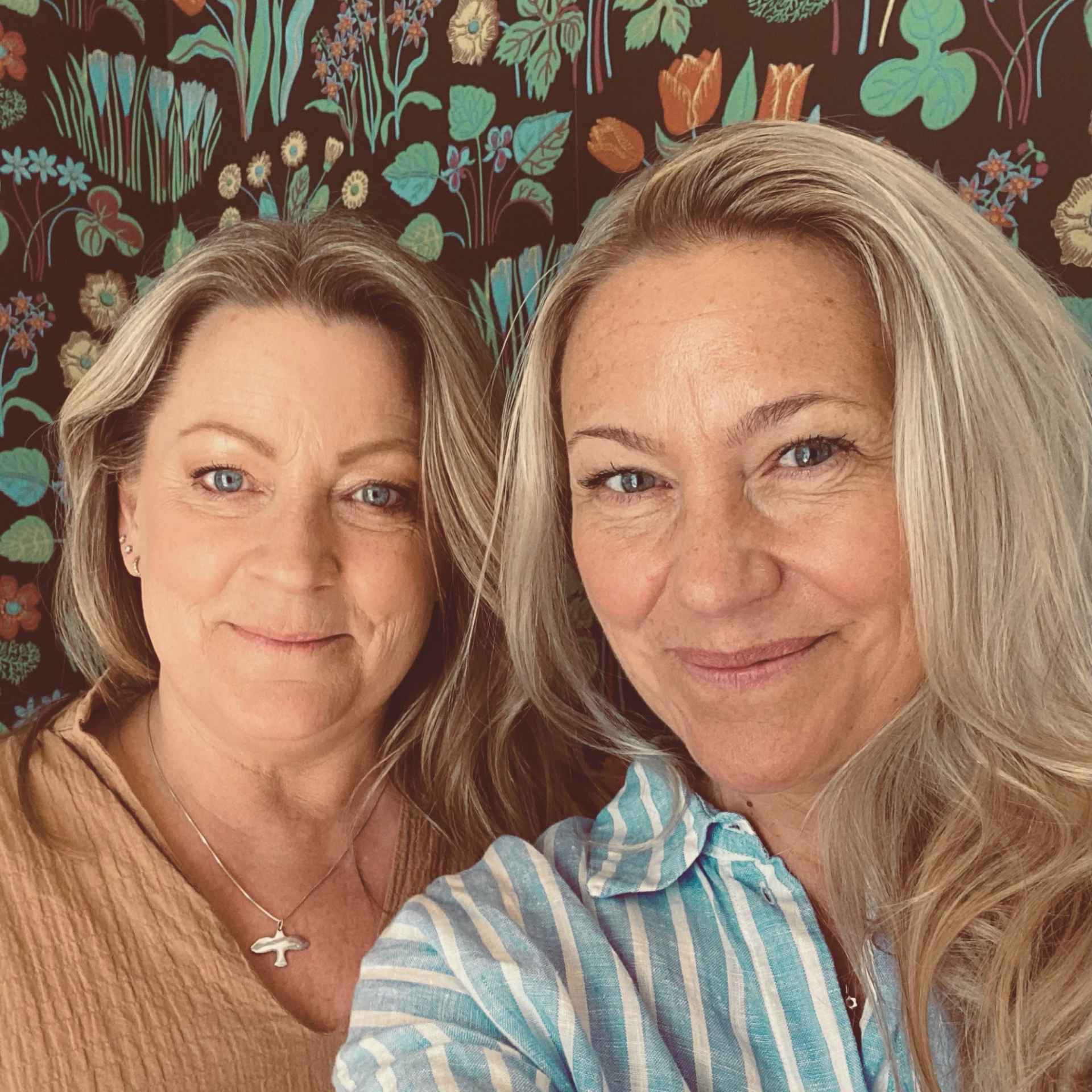 Jenny Berg och Frida Johansson i närbild, leende, framför färgglad blommig tapet.